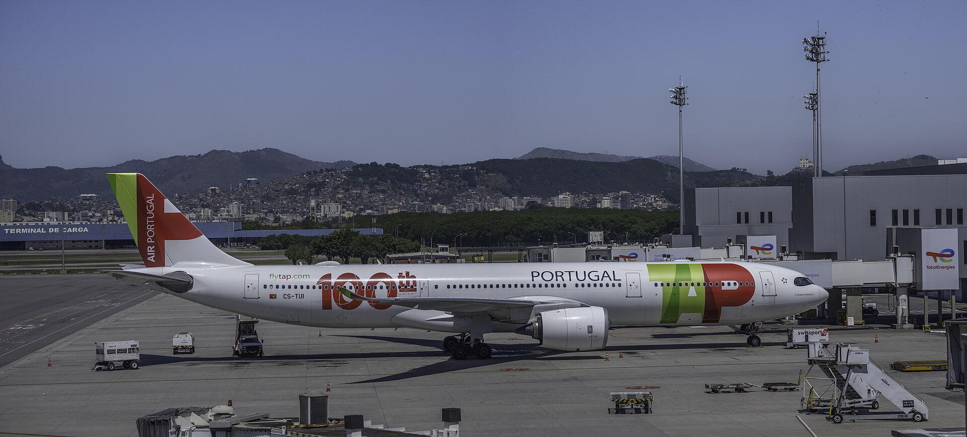 A white TAP Air Portugal wide-body jet parked on the apron at Galeão airport with Rio's hills behind