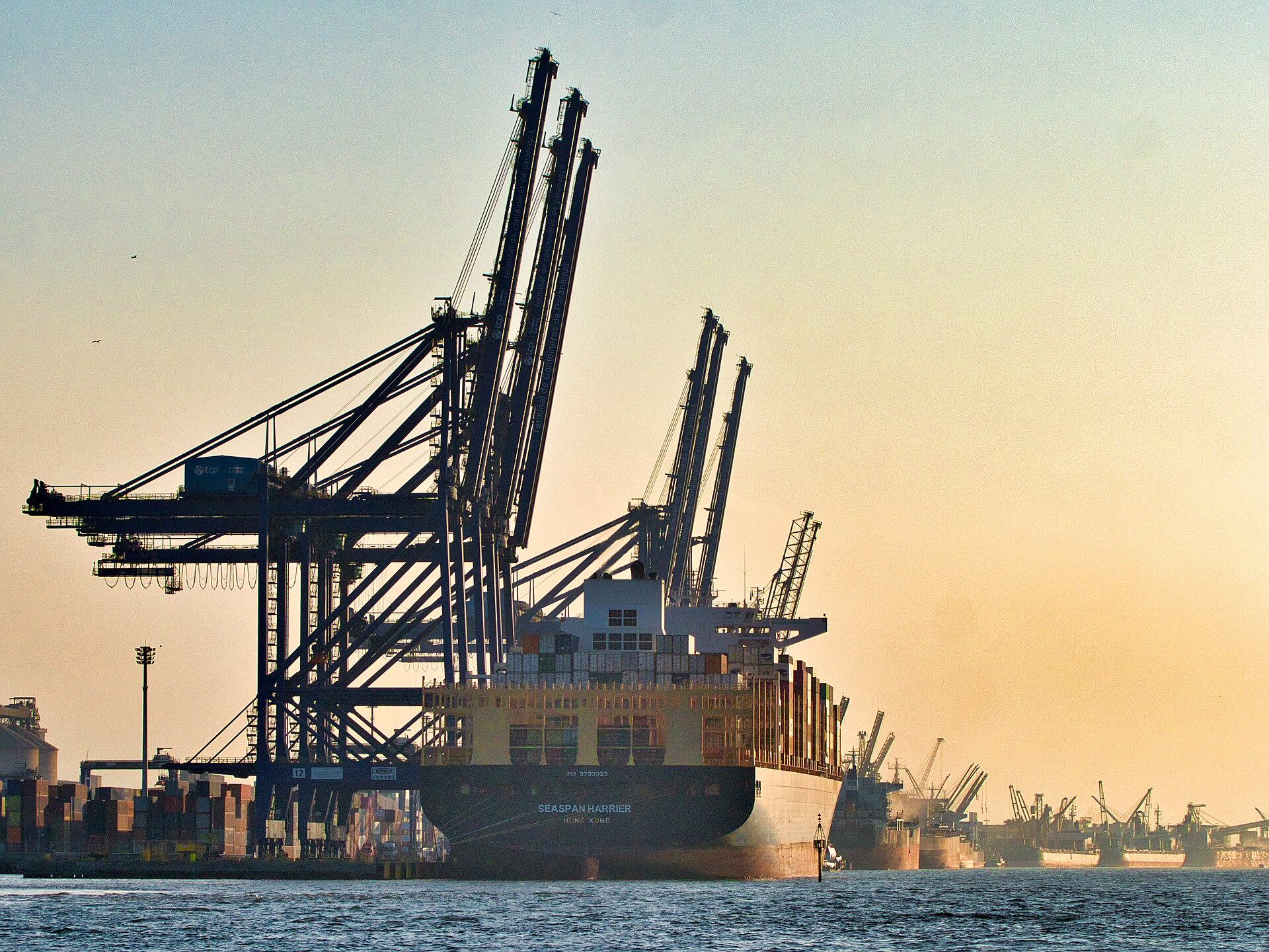 Container cranes and a large ship moored at the port of Paranaguá at sunset