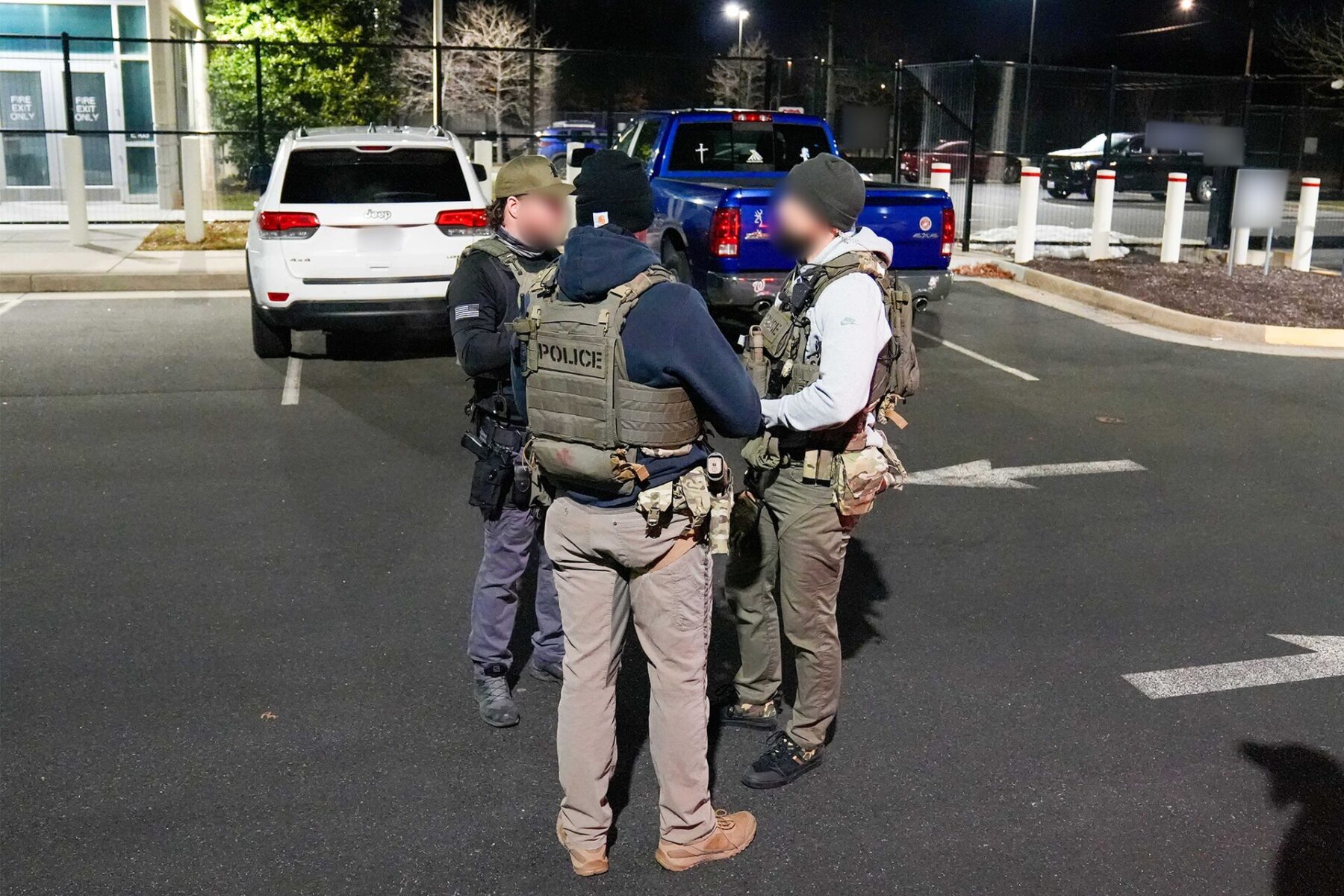US immigration officers in tactical vests stand in a parking lot at night next to vehicles