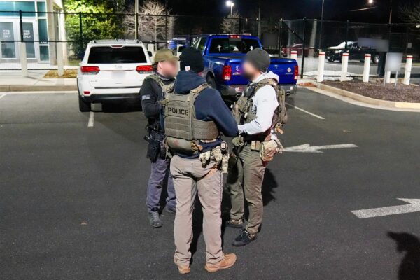 US immigration officers in tactical vests stand in a parking lot at night next to vehicles