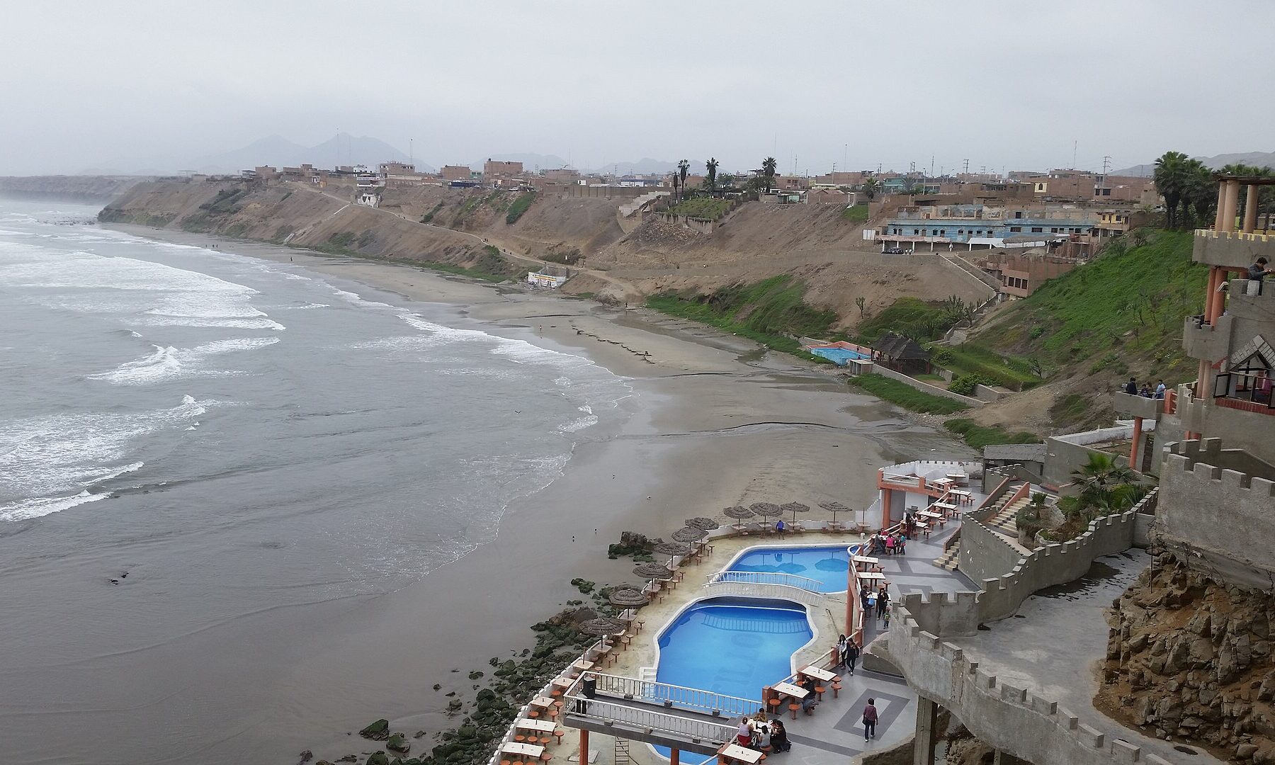 The coast of Chancay north of Lima with grey surf, a beach, cliff-top houses and swimming pools