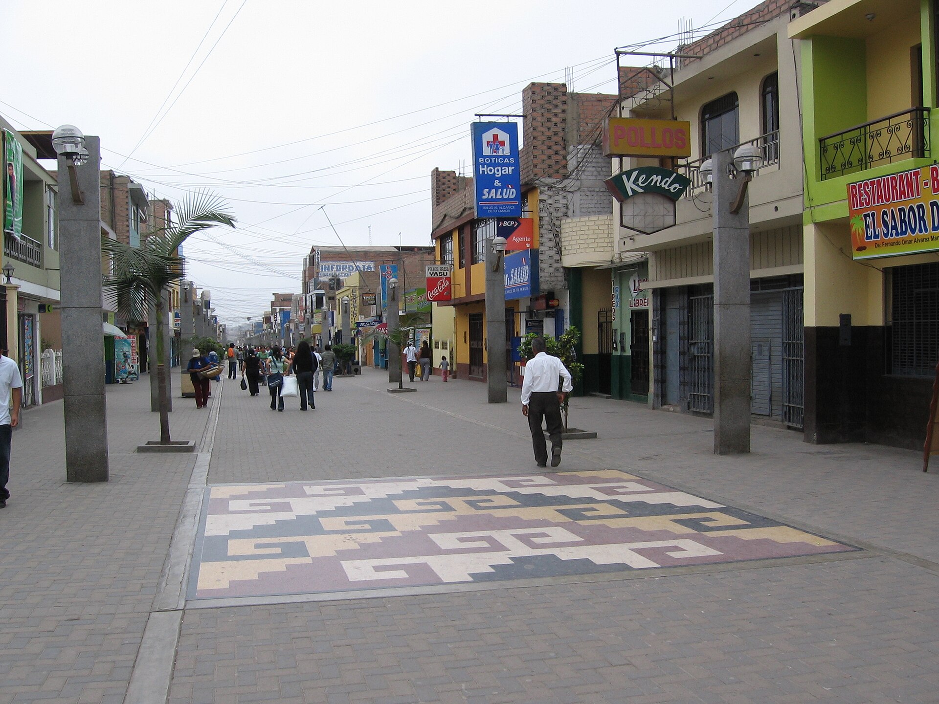 A pedestrian street in Chancay with patterned paving, shops and people walking