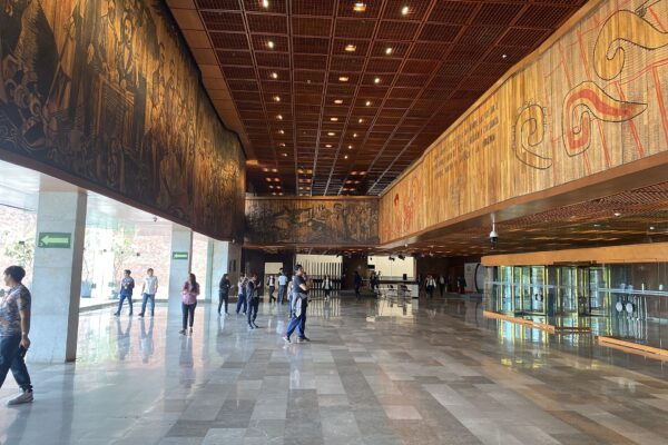 The marble lobby of Mexico's San Lázaro Legislative Palace with large carved murals on the walls and visitors walking