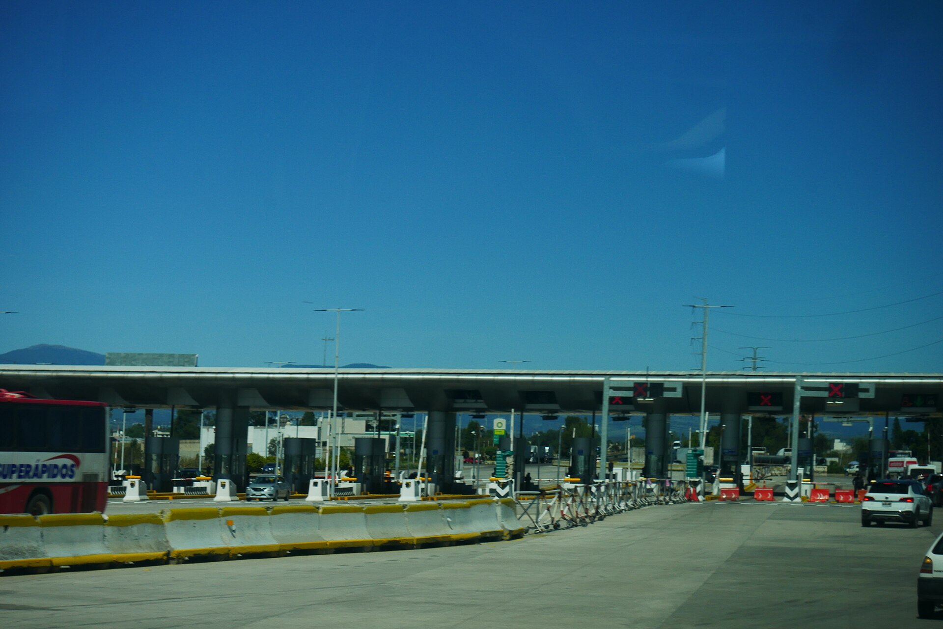 Toll booths of the Mexico–Puebla highway at Huejotzingo under a blue sky, with cars and a bus approaching