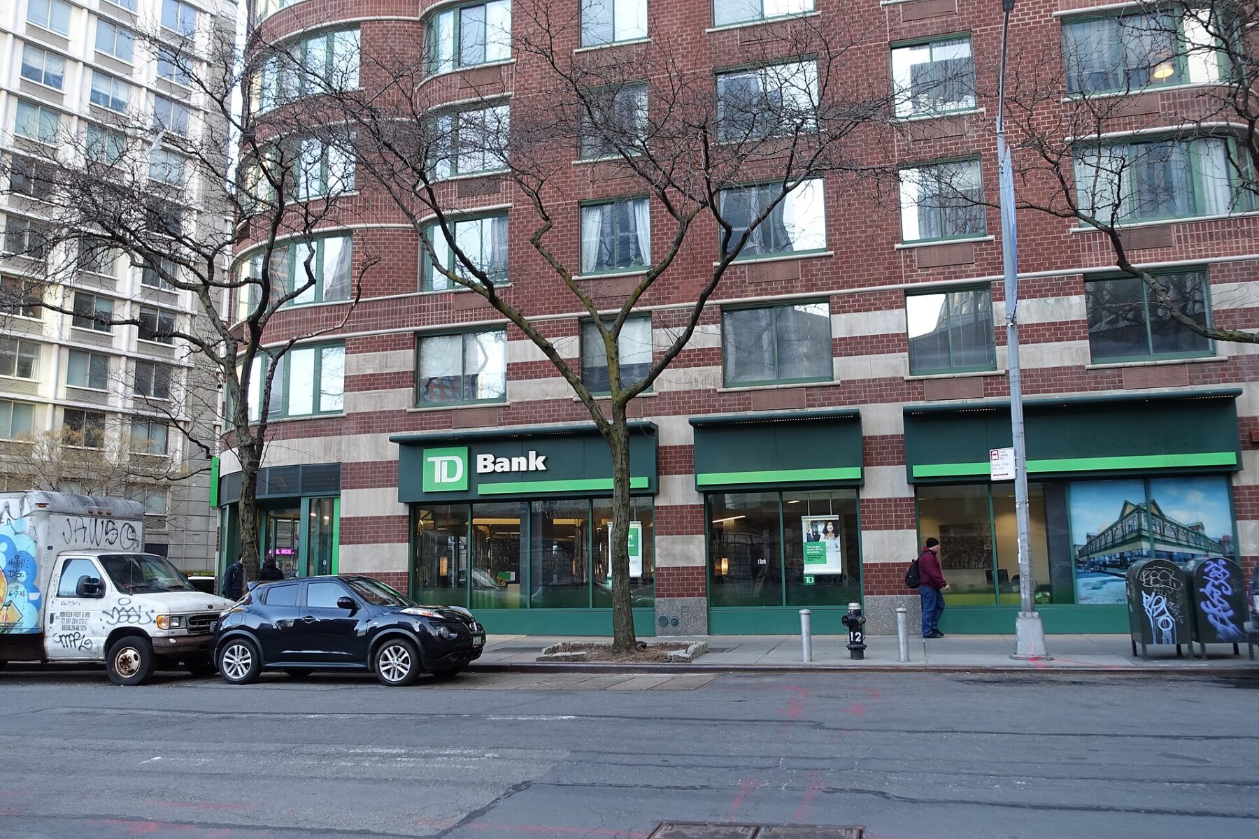 A TD Bank branch with green signs on the ground floor of a red-brick building on a New York street corner