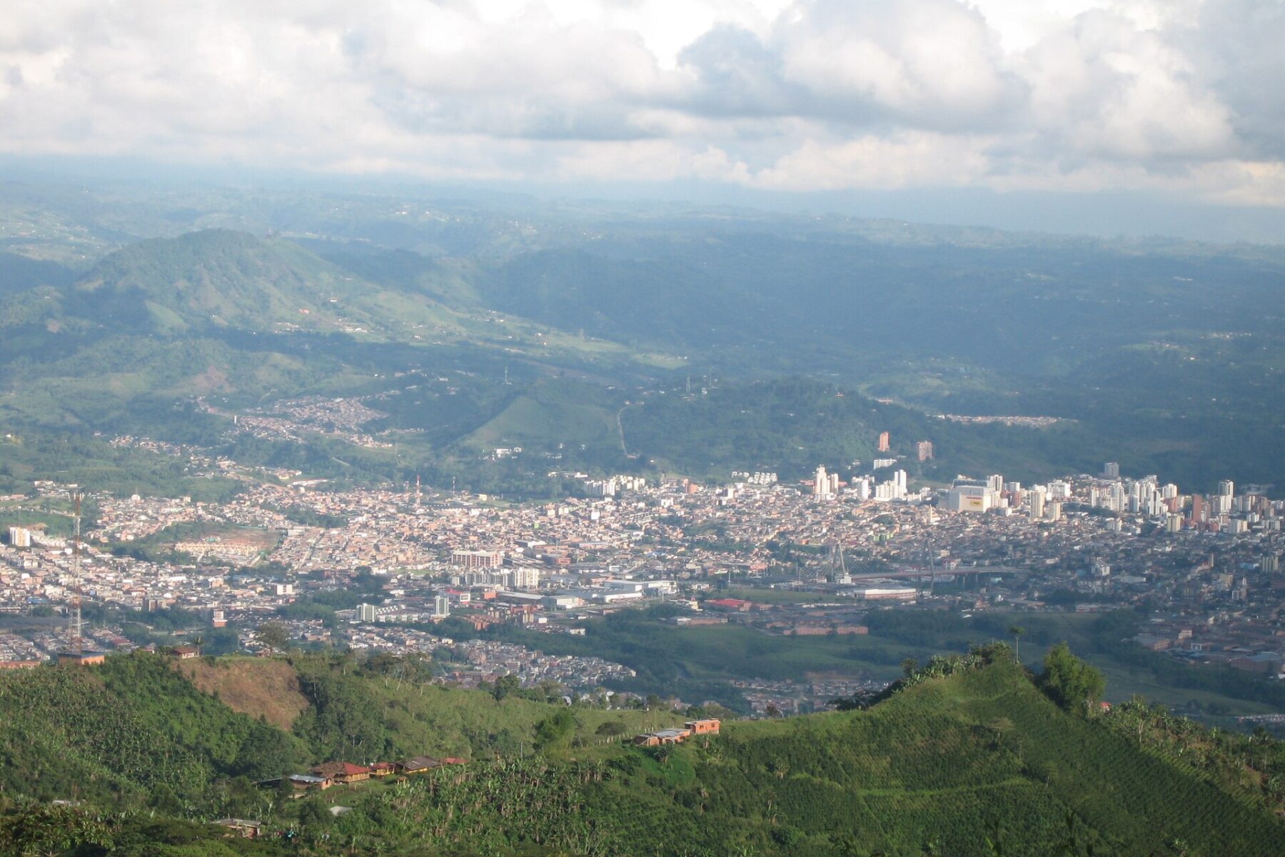 Panoramic view of the city of Pereira spread across a green valley with mountains behind under clouds