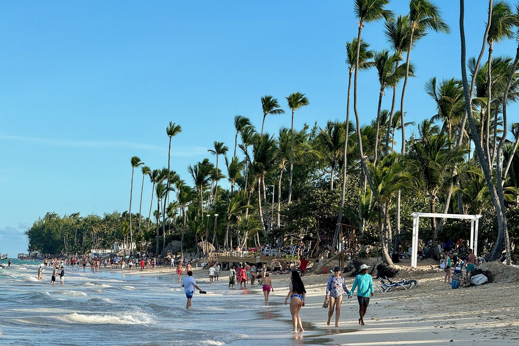 Tourists walking along Bávaro beach in Punta Cana with tall palm trees and turquoise water