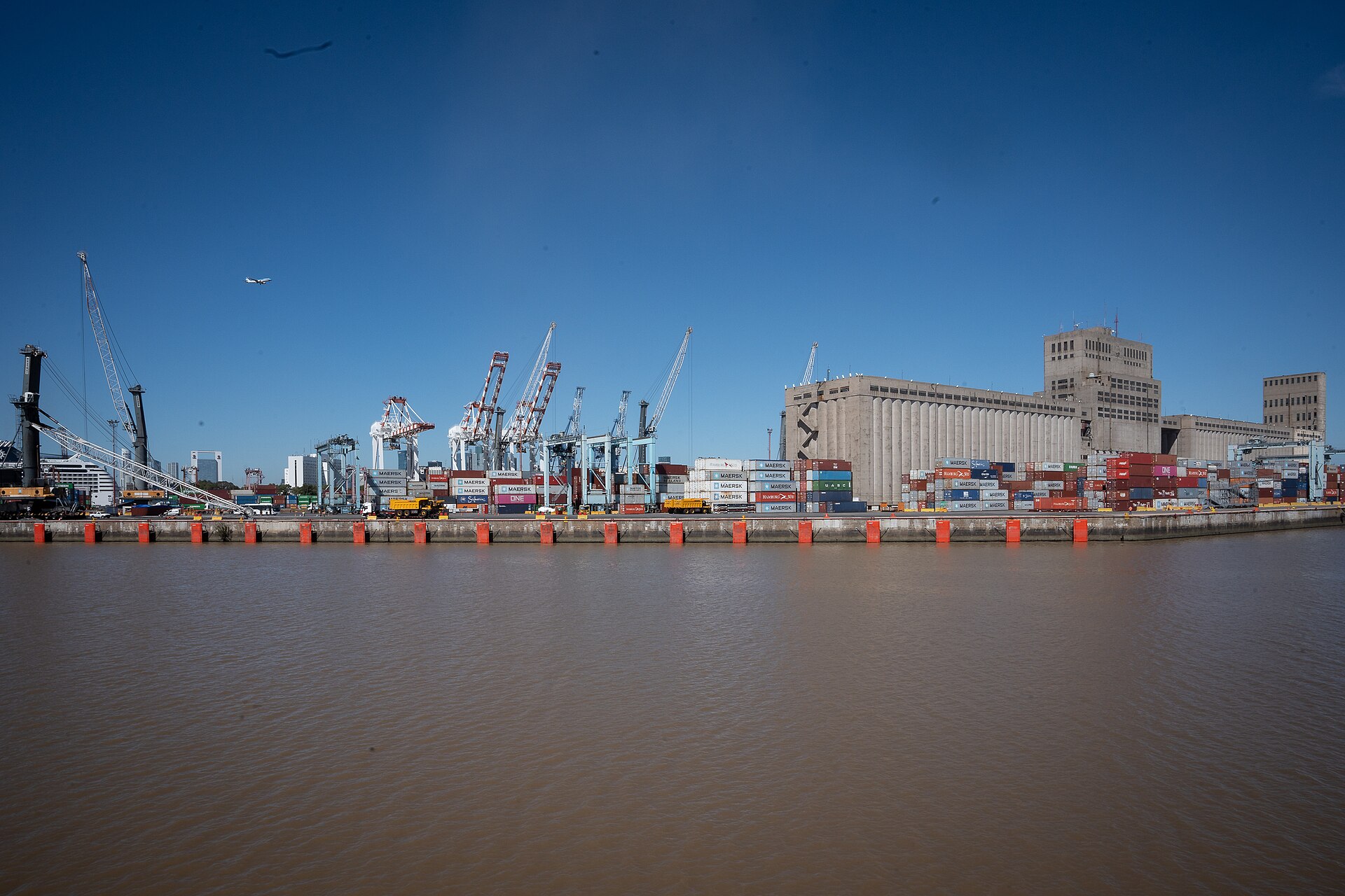 Container cranes and stacked containers at the port of Buenos Aires across brown river water