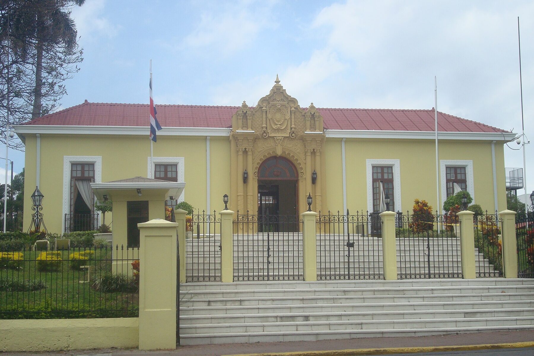 The yellow neocolonial Casa Amarilla in San José, Costa Rica, with an ornate entrance, steps and a Costa Rican flag