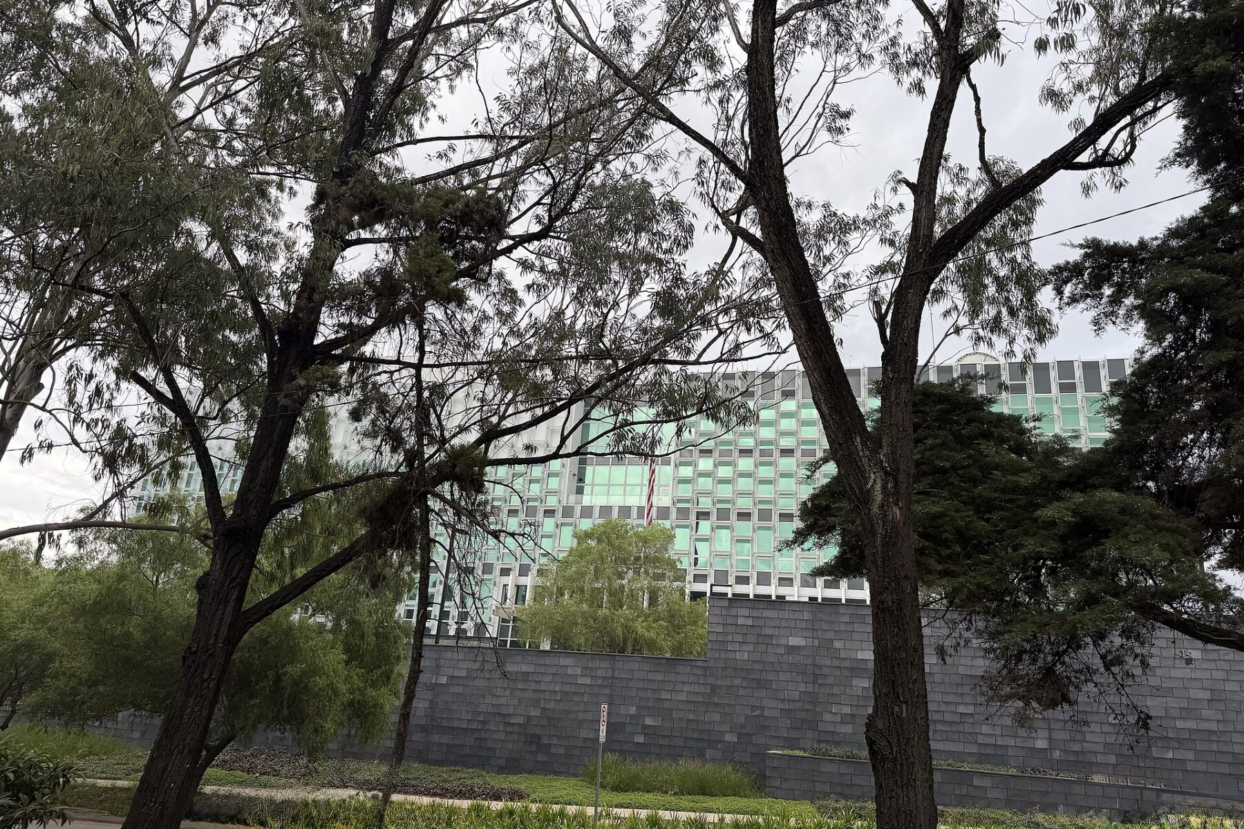 The green-glass US Embassy building in Guatemala City behind trees and a dark perimeter wall