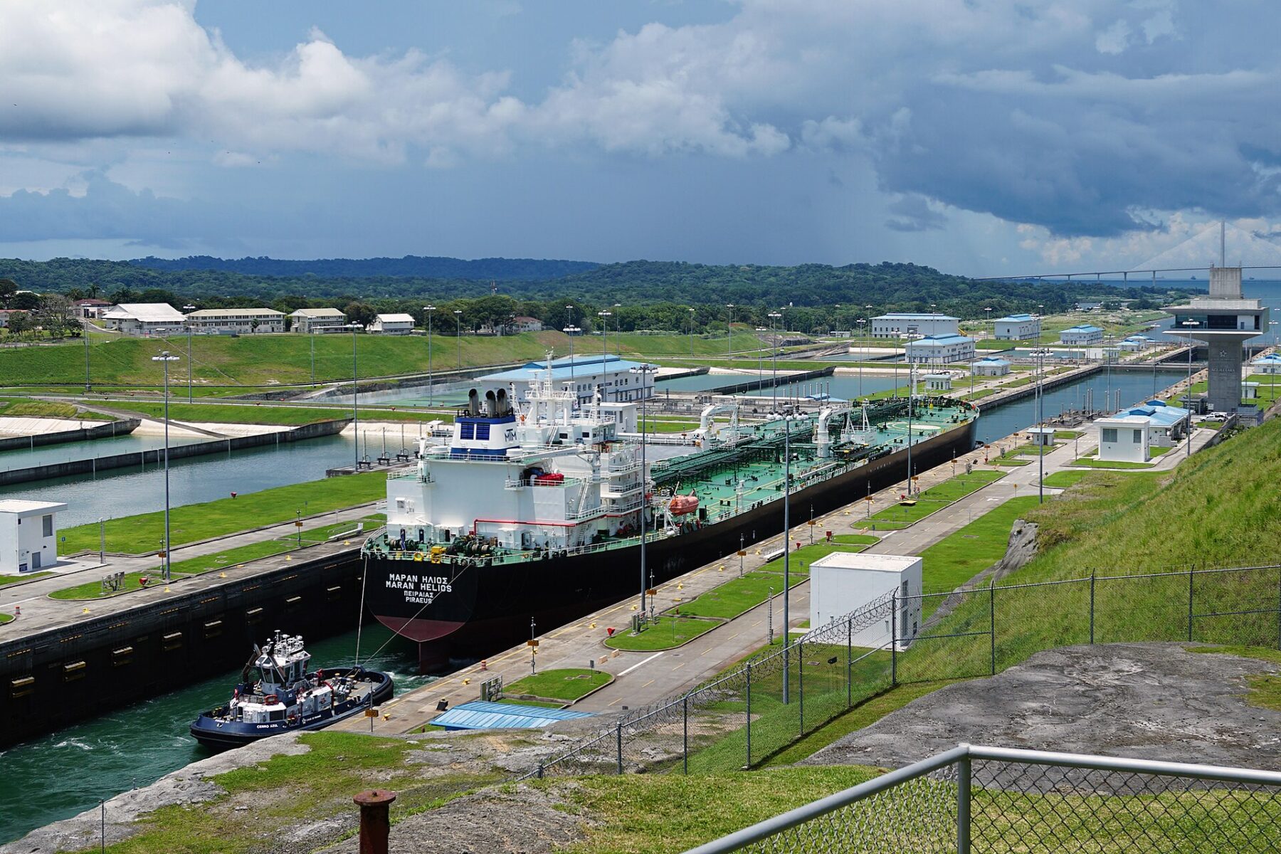 A tanker guided by a tug through the Agua Clara locks of the Panama Canal under a cloudy sky