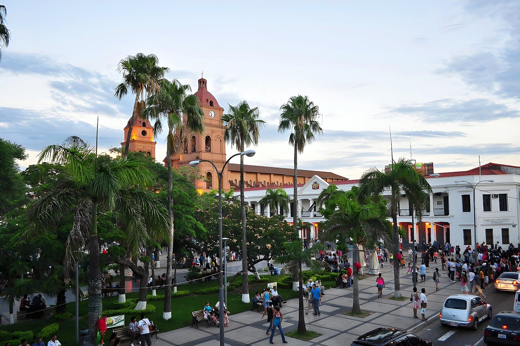 Plaza 24 de Septiembre in Santa Cruz de la Sierra with palm trees, people and the red-brick cathedral at dusk