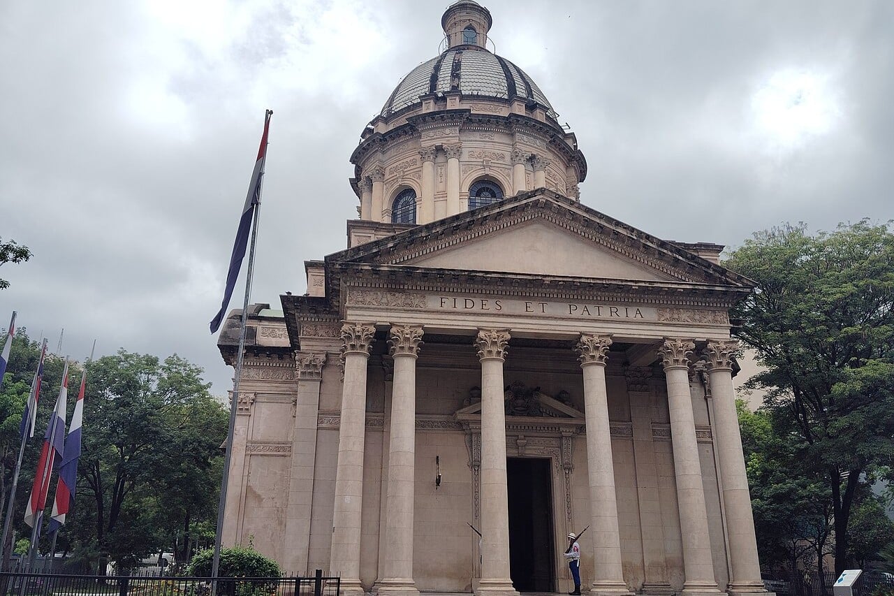 The domed National Pantheon of the Heroes in Asunción, Paraguay, with a guard at the entrance and Paraguayan flags on the left