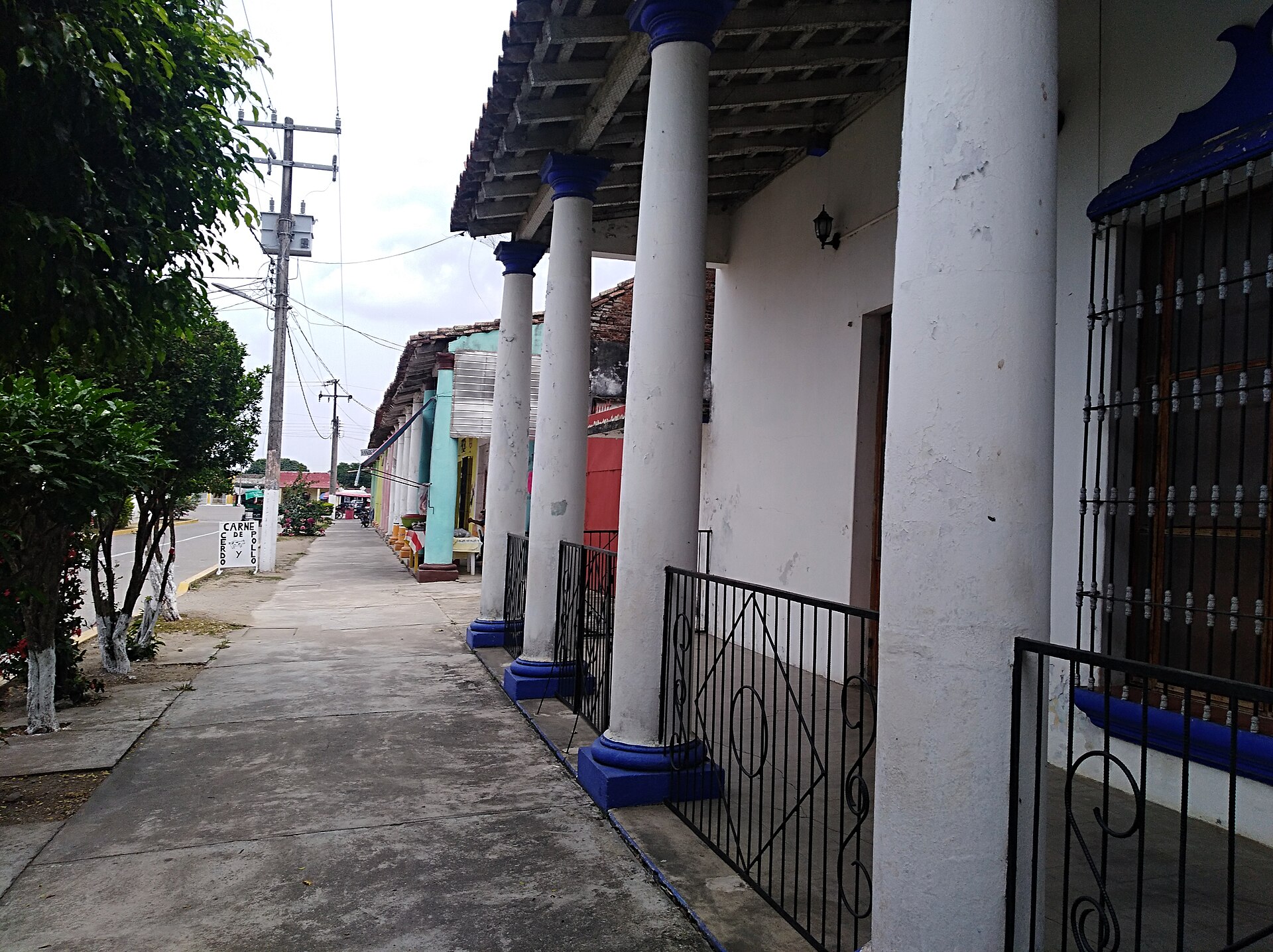 Empty pavement beside a row of white columns with blue bases and iron railings on a street in Otatitlán