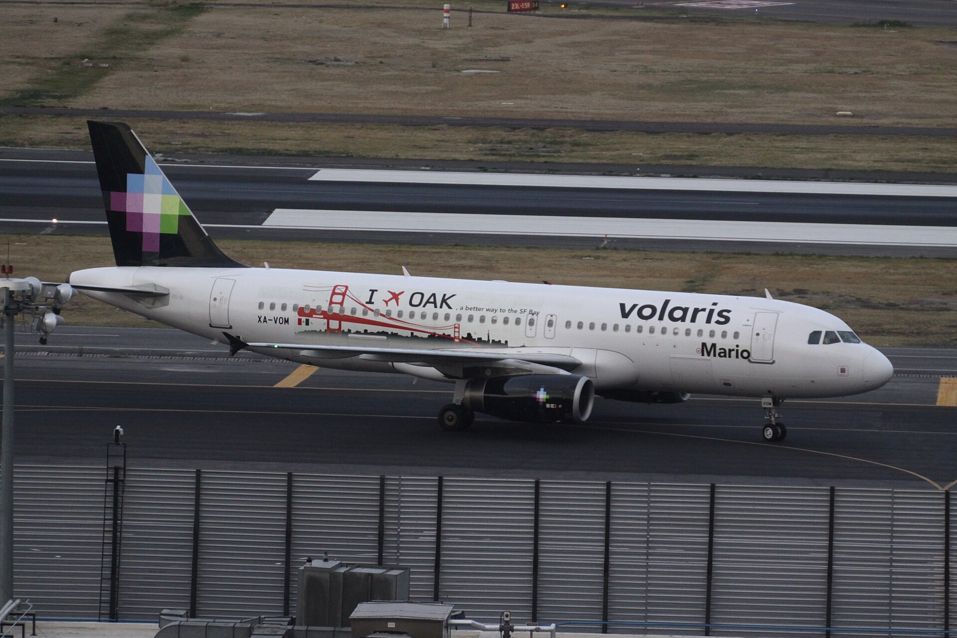 A white Volaris Airbus A320 with a black tail and a pixel-pattern logo taxiing on a runway at Mexico City International Airport