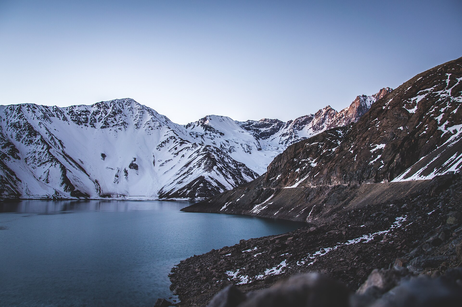 A deep blue reservoir below snow covered Andean peaks at dusk