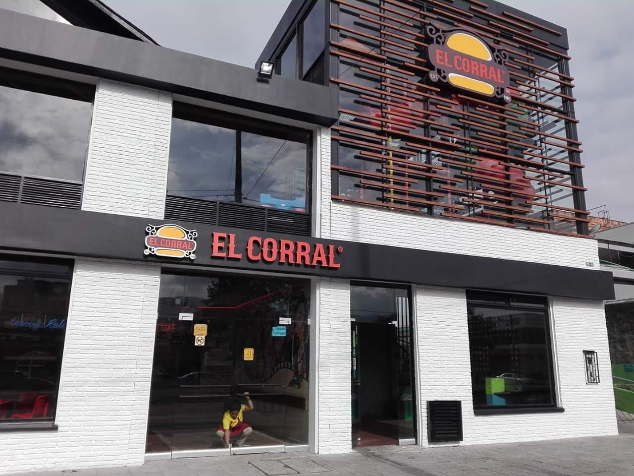 White-brick two-storey El Corral restaurant with red lettering and a wooden slat facade, a child crouching at the glass door