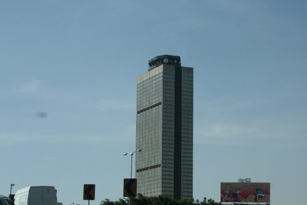 The Pemex headquarters tower in Mexico City rising above traffic signs and a van under a hazy blue sky