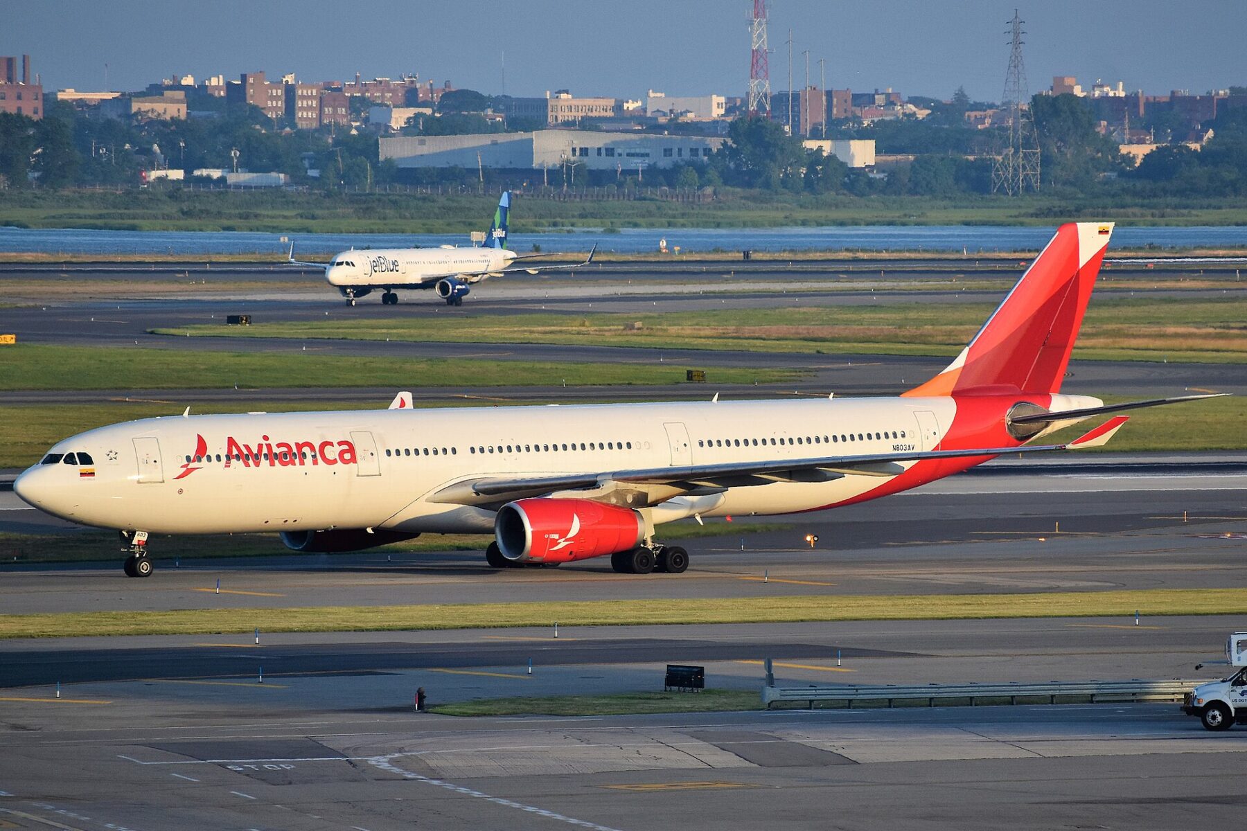 A red and white Avianca Airbus A330 taxiing at New York's JFK airport with a JetBlue jet behind it