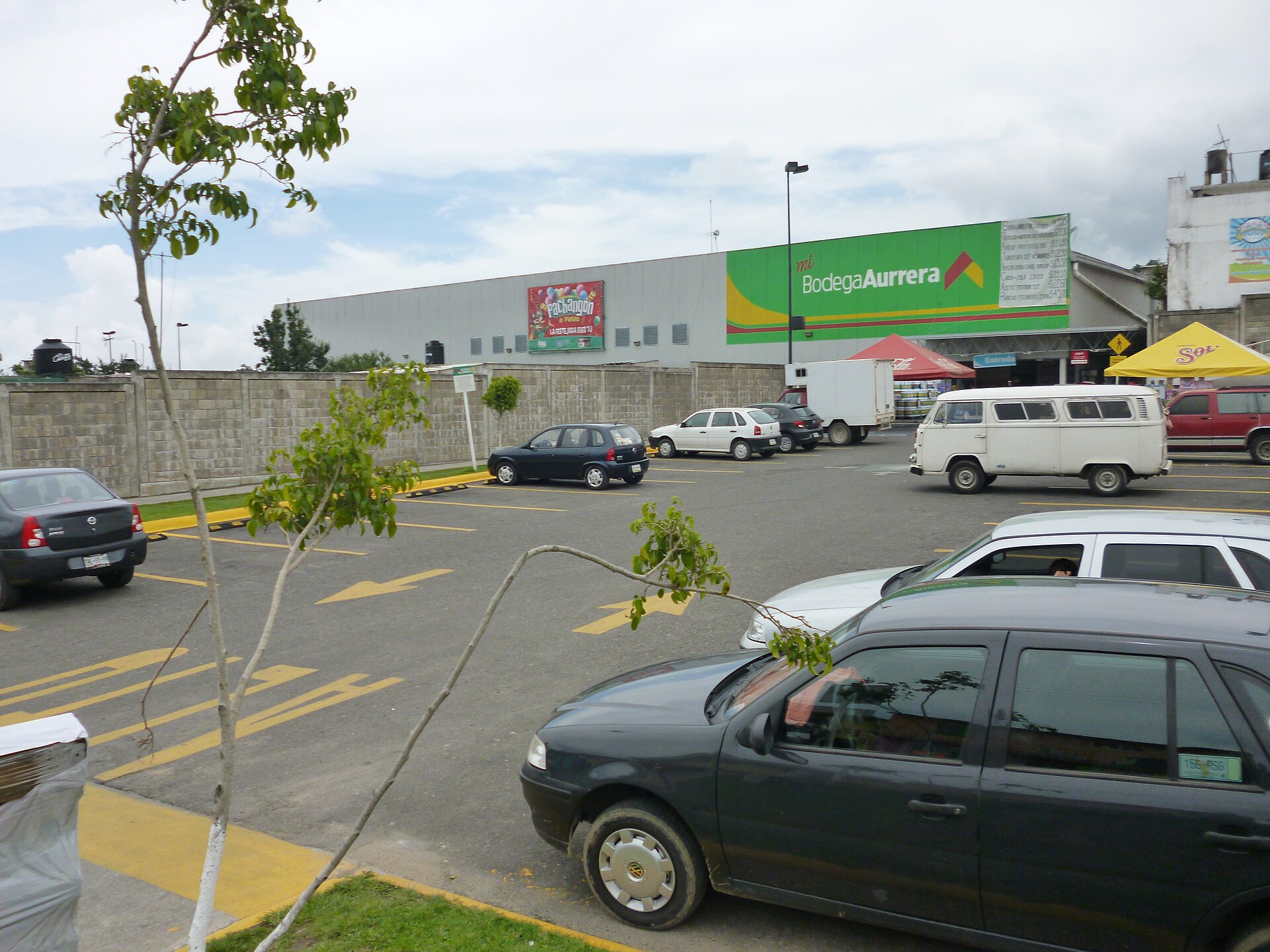 A Bodega Aurrera discount store with a green sign, a parking lot with cars and a white van in front