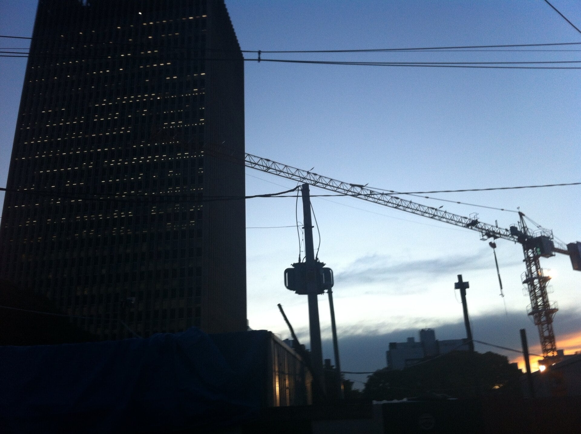 A dark Cemig office tower in Belo Horizonte at dusk, with power lines, a transformer pole and a construction crane in front of the sky