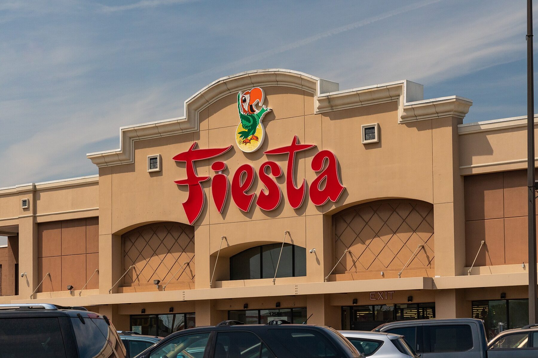 The front of a Fiesta Mart supermarket in Houston, Texas, with the red Fiesta sign and a parrot logo above a car park with parked vehicles
