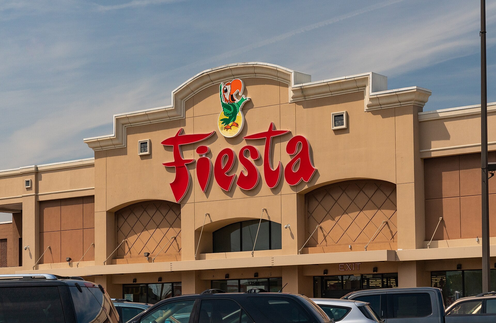 The front of a Fiesta Mart supermarket in Houston, Texas, with the red Fiesta sign and a parrot logo above a car park with parked vehicles