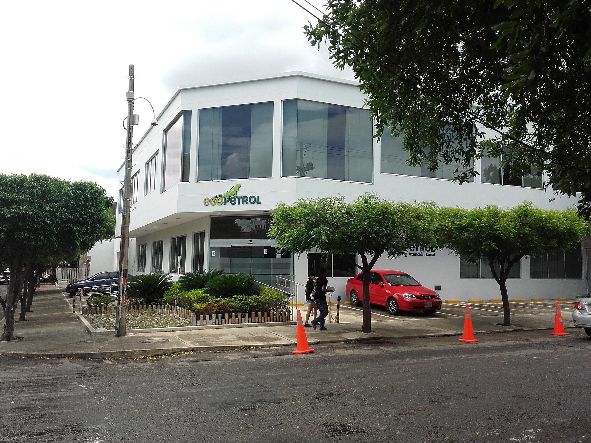 A white two-storey Ecopetrol office building with the green Ecopetrol logo on a street corner in Cucuta, trees and a red car in front