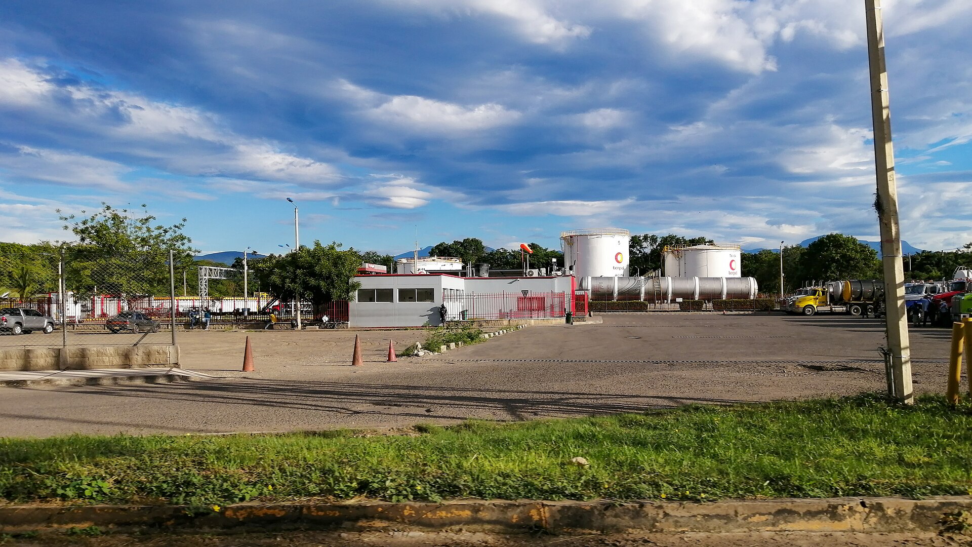 Fuel storage tanks and a loading yard with tanker trucks under a blue cloudy sky