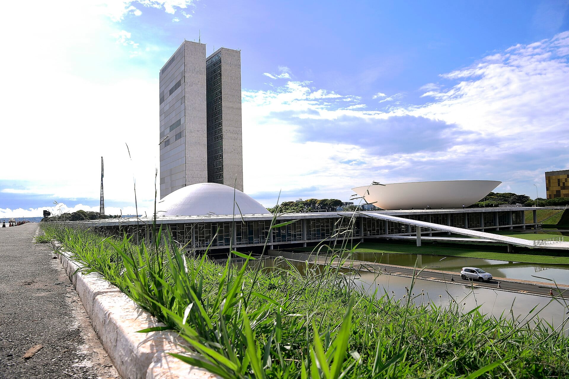 The twin office towers, white dome and upturned bowl of Brazil's National Congress in Brasília behind tall grass and a strip of water