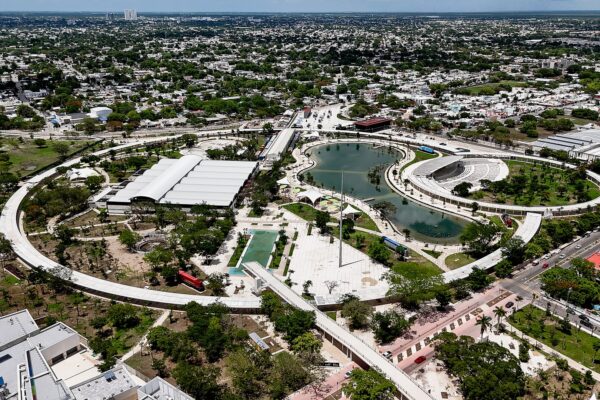 Aerial view of a large city park in Mérida with a curved lake, a ring-shaped walkway and an amphitheatre, surrounded by houses and trees