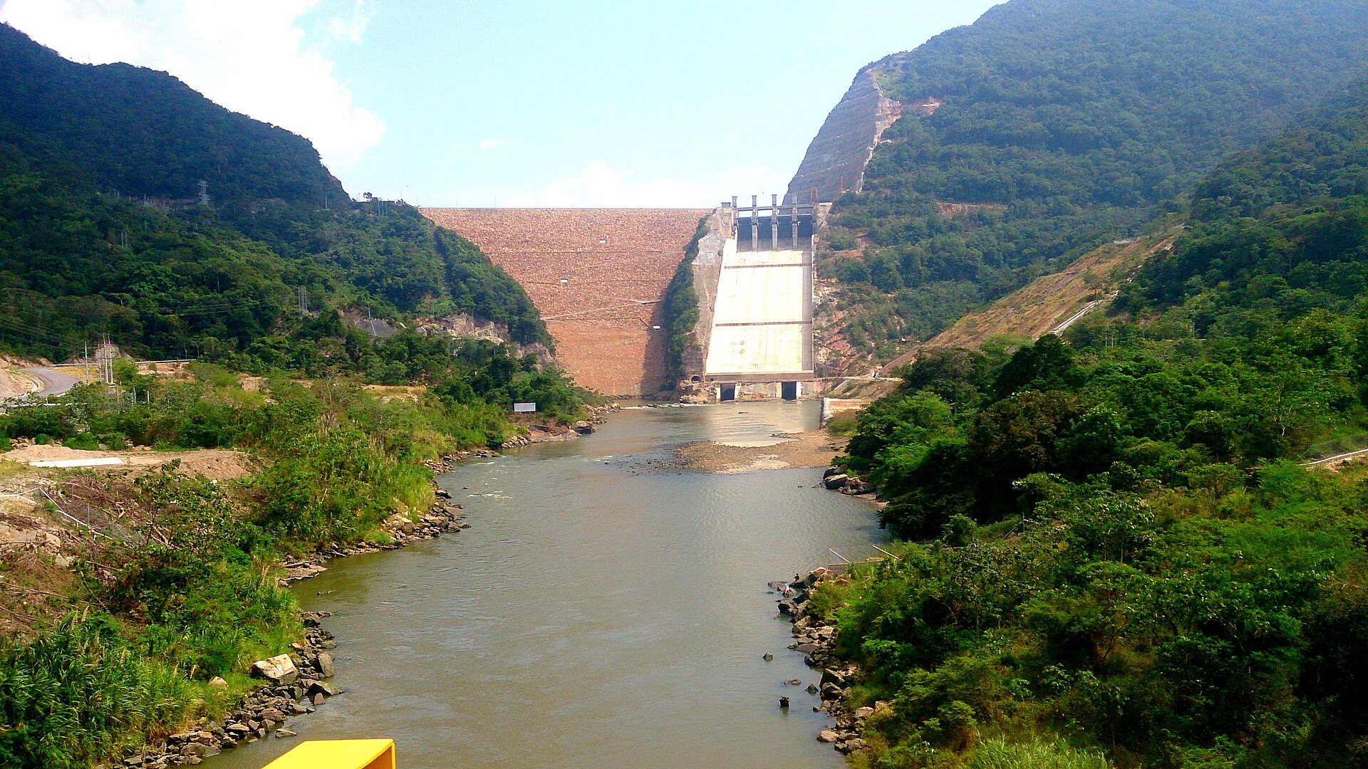 The rockfill dam and concrete spillway of the Sogamoso hydropower plant in Santander, Colombia, with the river and green hills in front