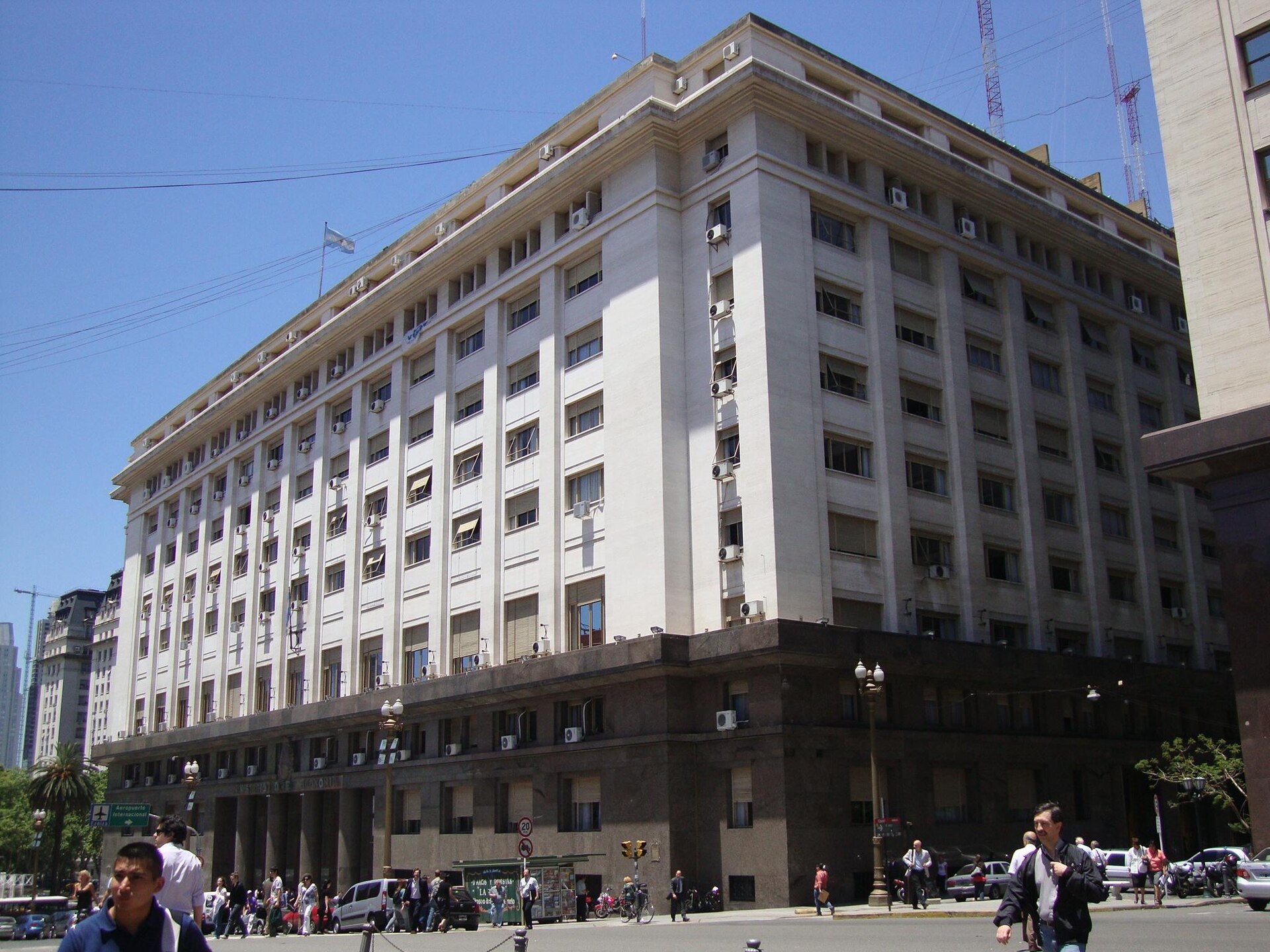 Large cream-coloured government building with rows of windows on a street corner in Buenos Aires, pedestrians and parked vans at street level