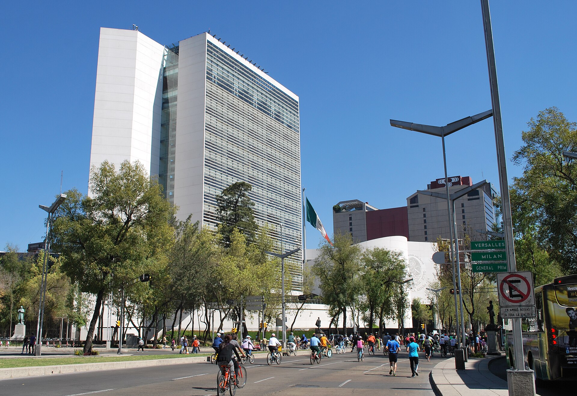 The Mexican Senate tower on Paseo de la Reforma under a blue sky, with cyclists and runners on the avenue in front