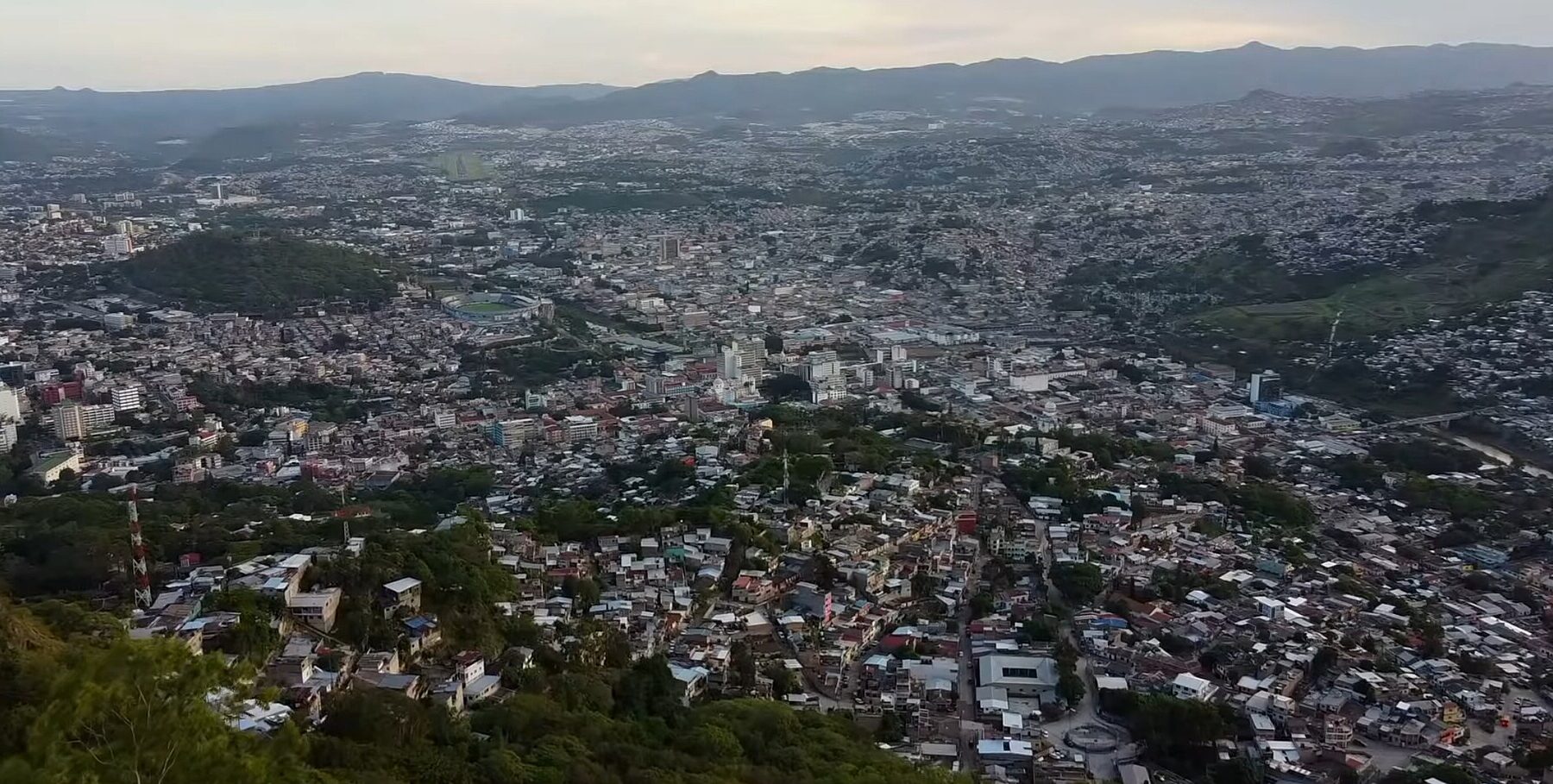 Elevated view of Tegucigalpa from a hillside, with dense neighbourhoods, green slopes and mountains on the horizon