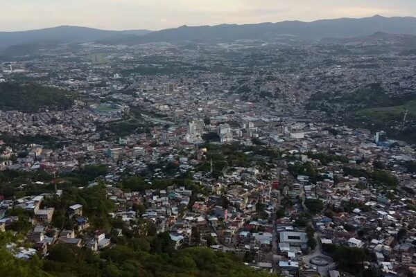 Elevated view of Tegucigalpa from a hillside, with dense neighbourhoods, green slopes and mountains on the horizon