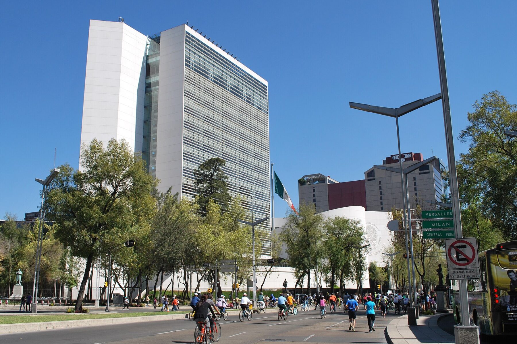 The Mexican Senate tower on Paseo de la Reforma under a blue sky, with cyclists and runners on the avenue in front