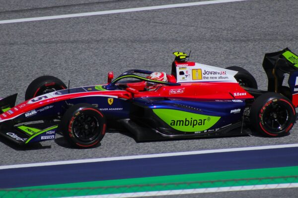 A blue, red and white Trident Formula 3 car with the number 5, a Ferrari Driver Academy logo and green sponsor panels drives along a grey track as the driver in a red and white helmet looks ahead