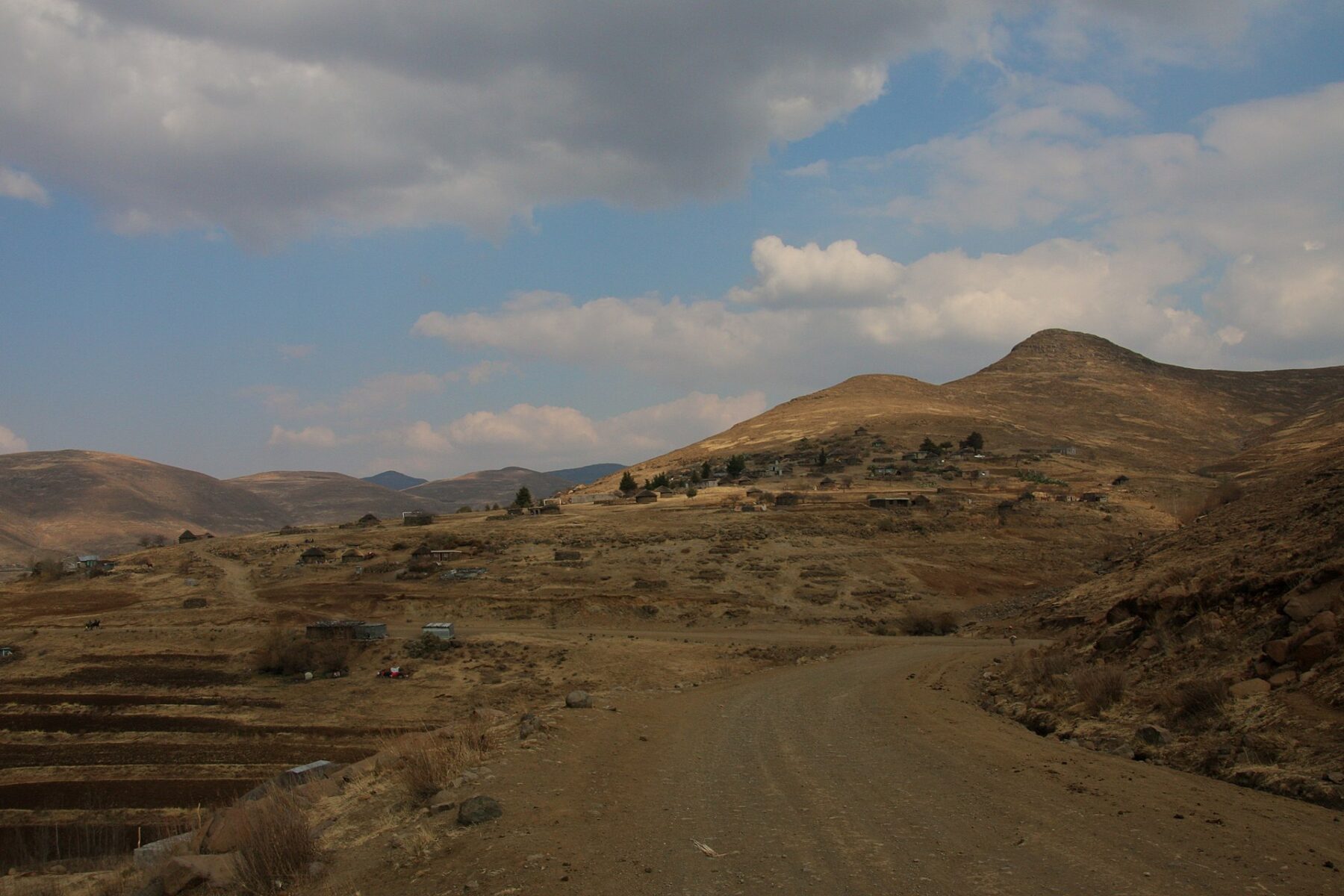 A gravel road winding through dry hills and villages in rural Lesotho