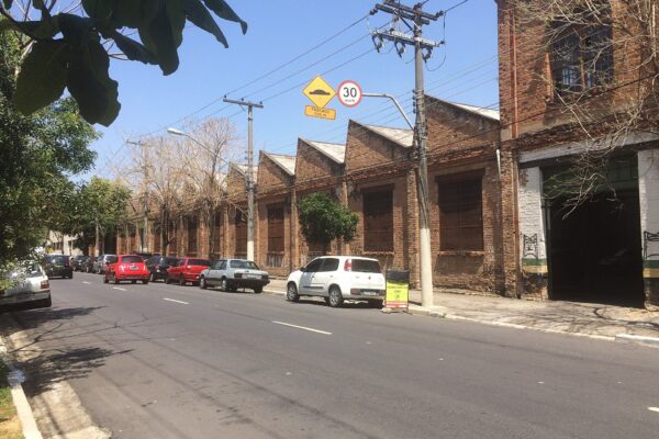 Row of brick industrial sheds with sawtooth roofs on a sunlit street in the Mooca district of São Paulo, Brazil