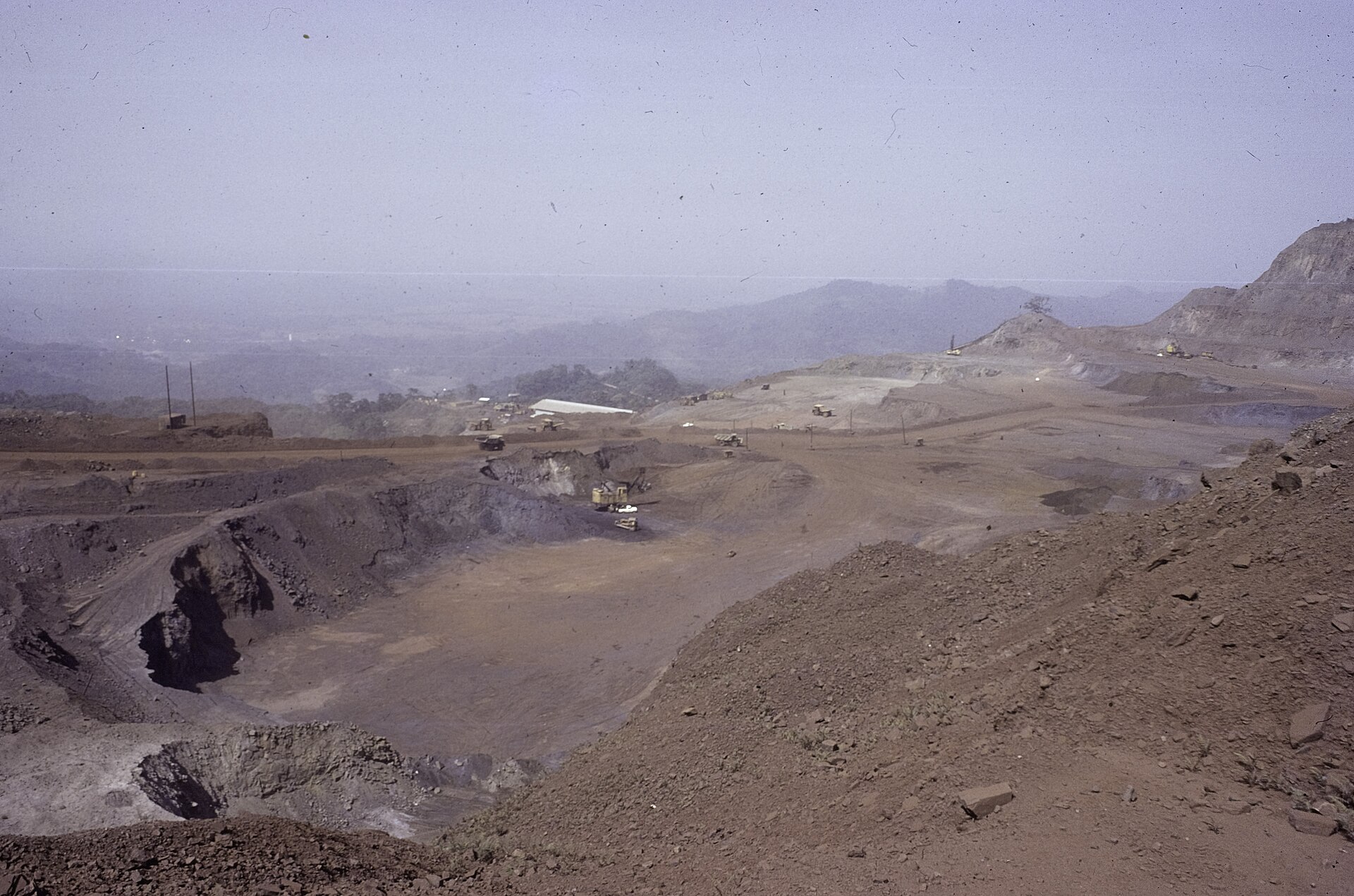 Open-pit iron ore mine with excavators and trucks at Yekepa in Nimba County, Liberia, with hills in the background