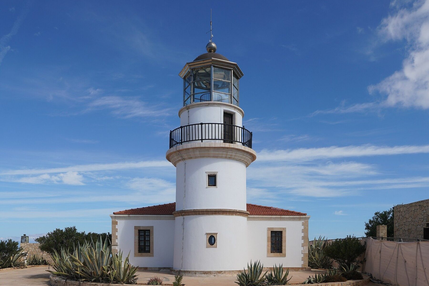 White lighthouse tower with a red-tiled keeper's house on Gavdos island, Greece's southernmost inhabited island, under a blue sky