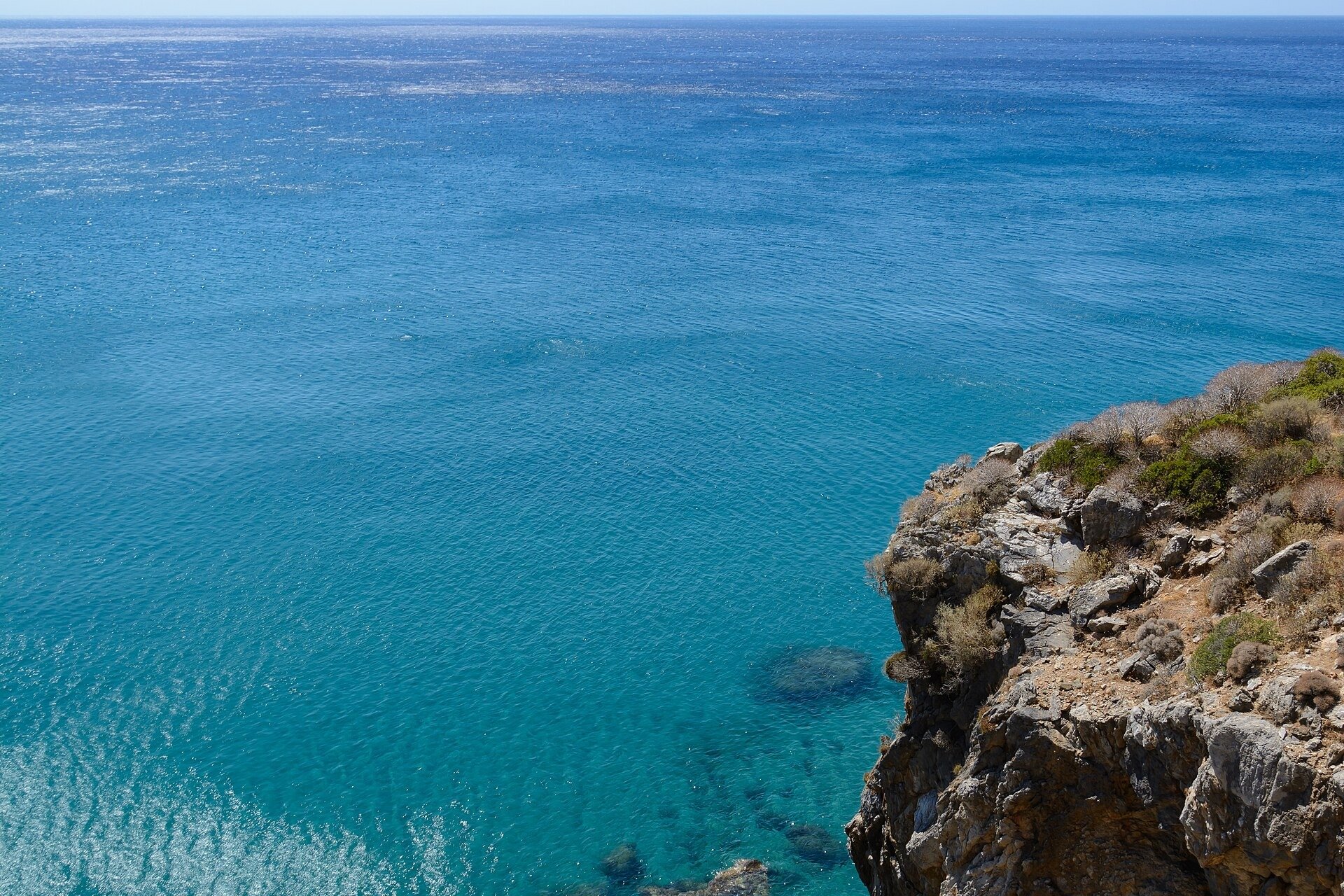 Open blue sea seen from a rocky cliff on the south coast of Crete, with the horizon of the Libyan Sea in the distance