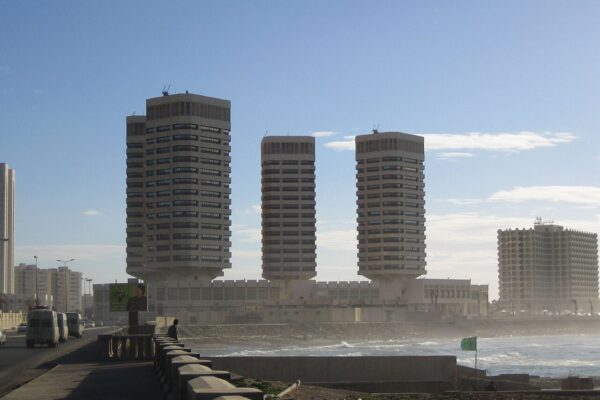 Three concrete office towers on the Tripoli seafront in Libya, with waves and a coastal road in the foreground