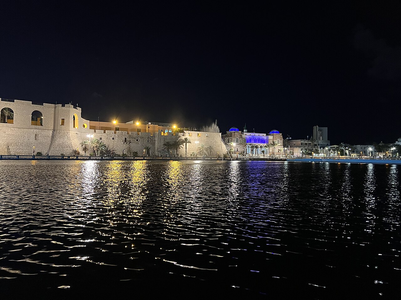 The walls of Tripoli's Red Castle and a lit building on the harbour front at night, seen across dark water