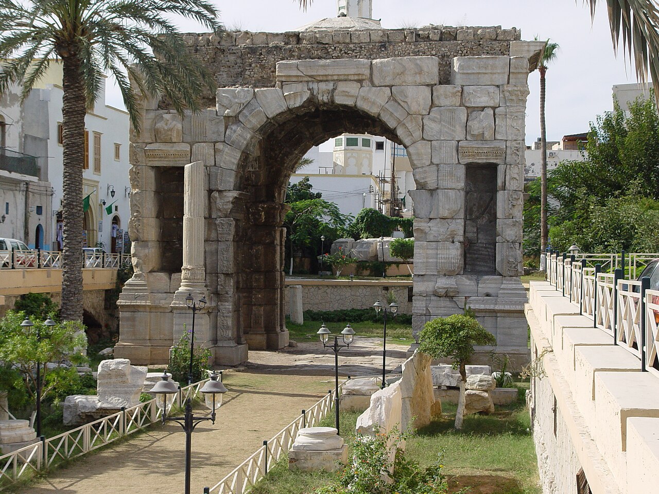 Roman marble triumphal arch in Tripoli, Libya, with palm trees, a stone path and street lamps around it