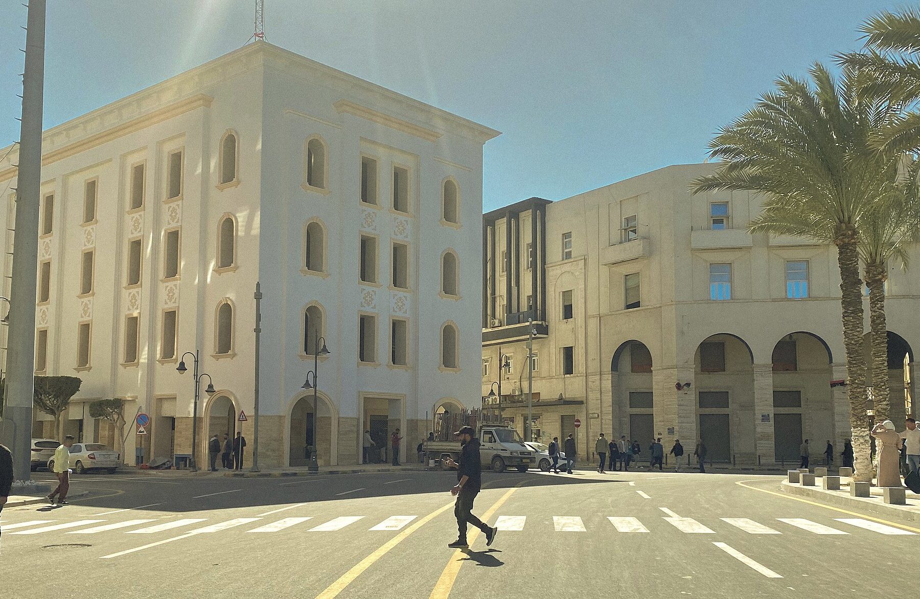 Pedestrians cross Martyrs' Square in central Tripoli, Libya, past white and cream-coloured buildings on a sunny day