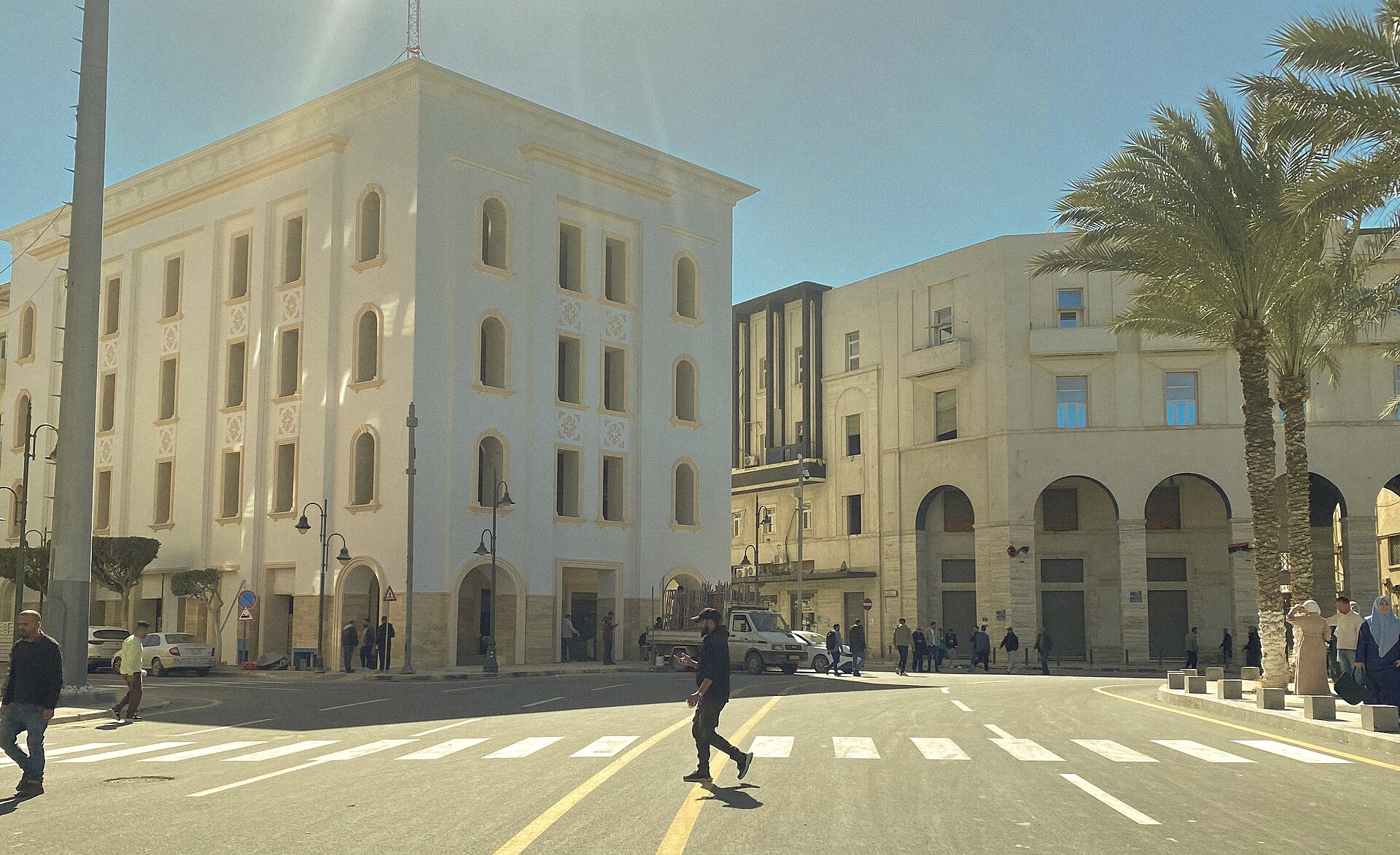 Pedestrians cross Martyrs' Square in central Tripoli, Libya, past white and cream-coloured buildings on a sunny day