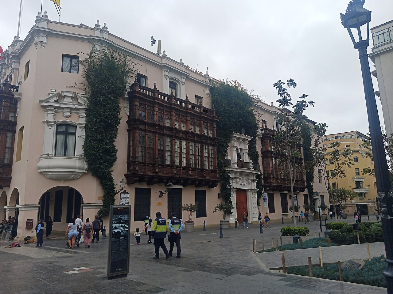Side wing of Lima's Municipal Palace with carved wooden balconies on Jirón Conde de Superunda, with pedestrians walking past