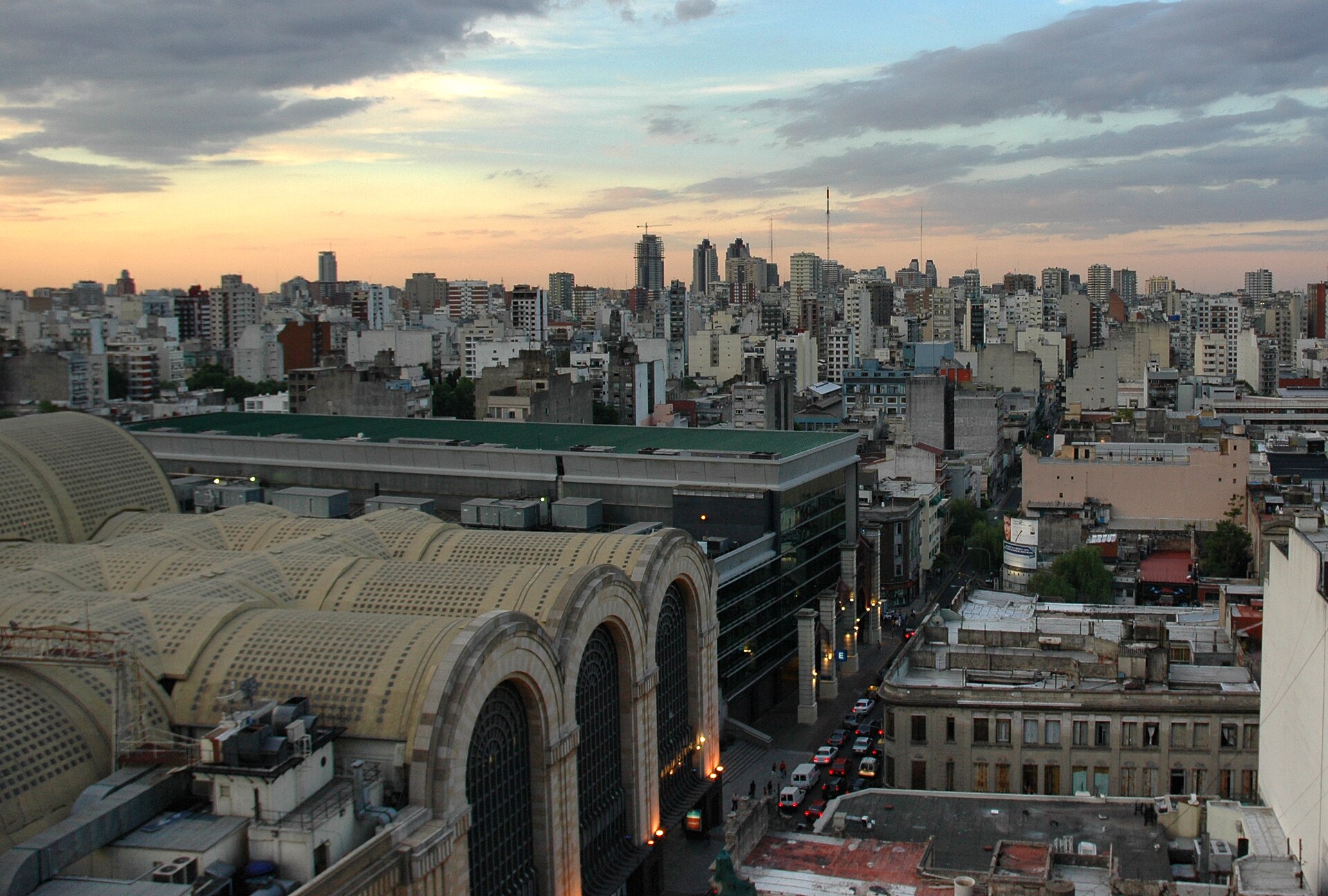 Dusk view over Buenos Aires rooftops with the vaulted roofs of the Abasto Shopping centre at left and a street running between apartment blocks